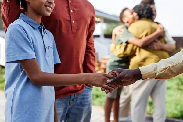 side view closeup young african american boy shaking hands with family member summer party